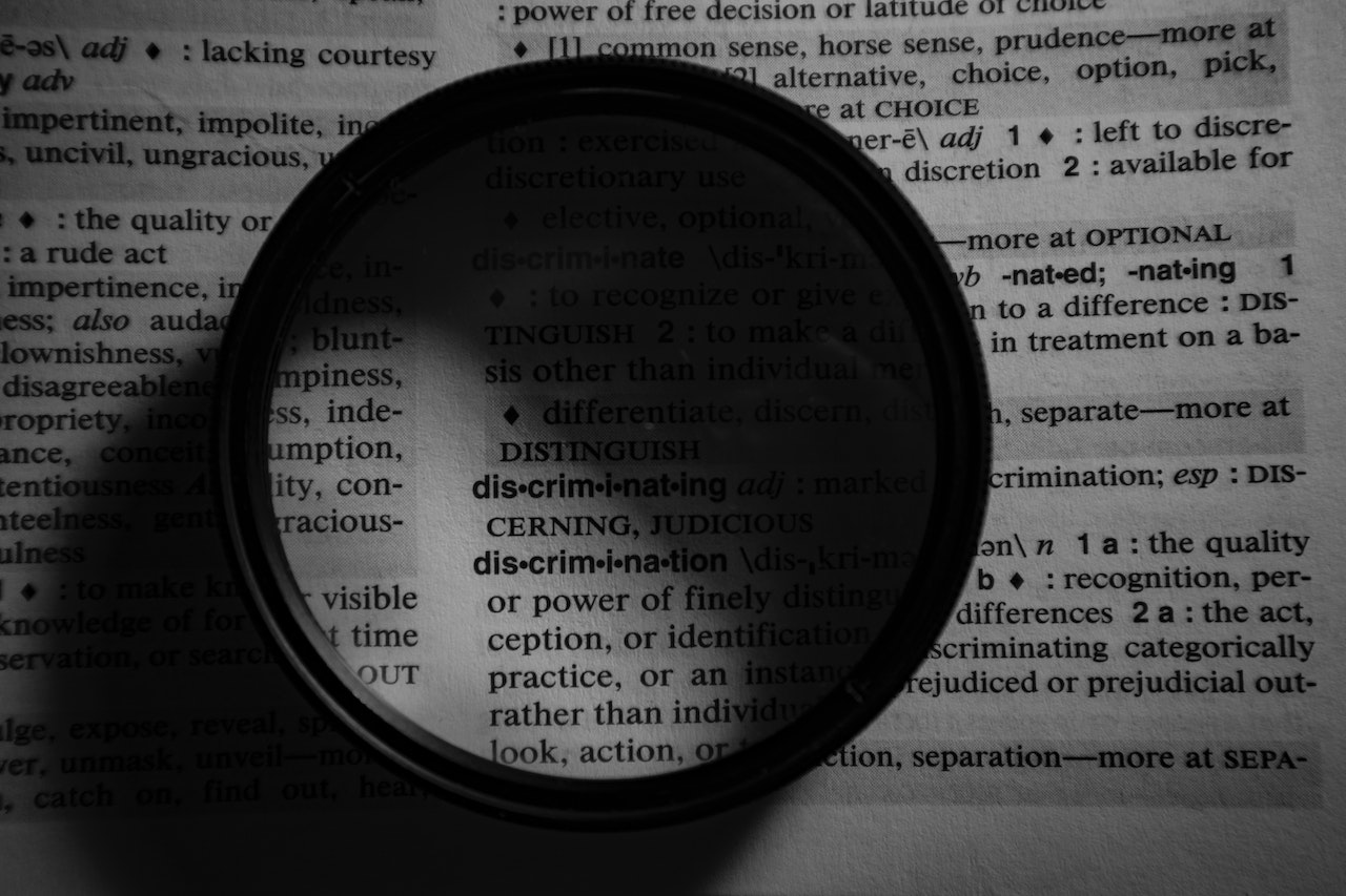 Stock photo of a page of a dictionary. Something round resembling a magnifying glass has been laid over the word "Discrimination" to draw attention to it.
